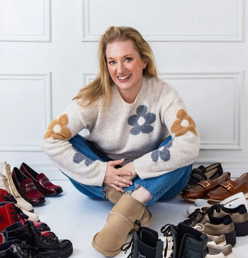 Claudine Péclet, owner of Escarpins et Vilebrequins, sitting among boots and shoes from her store.