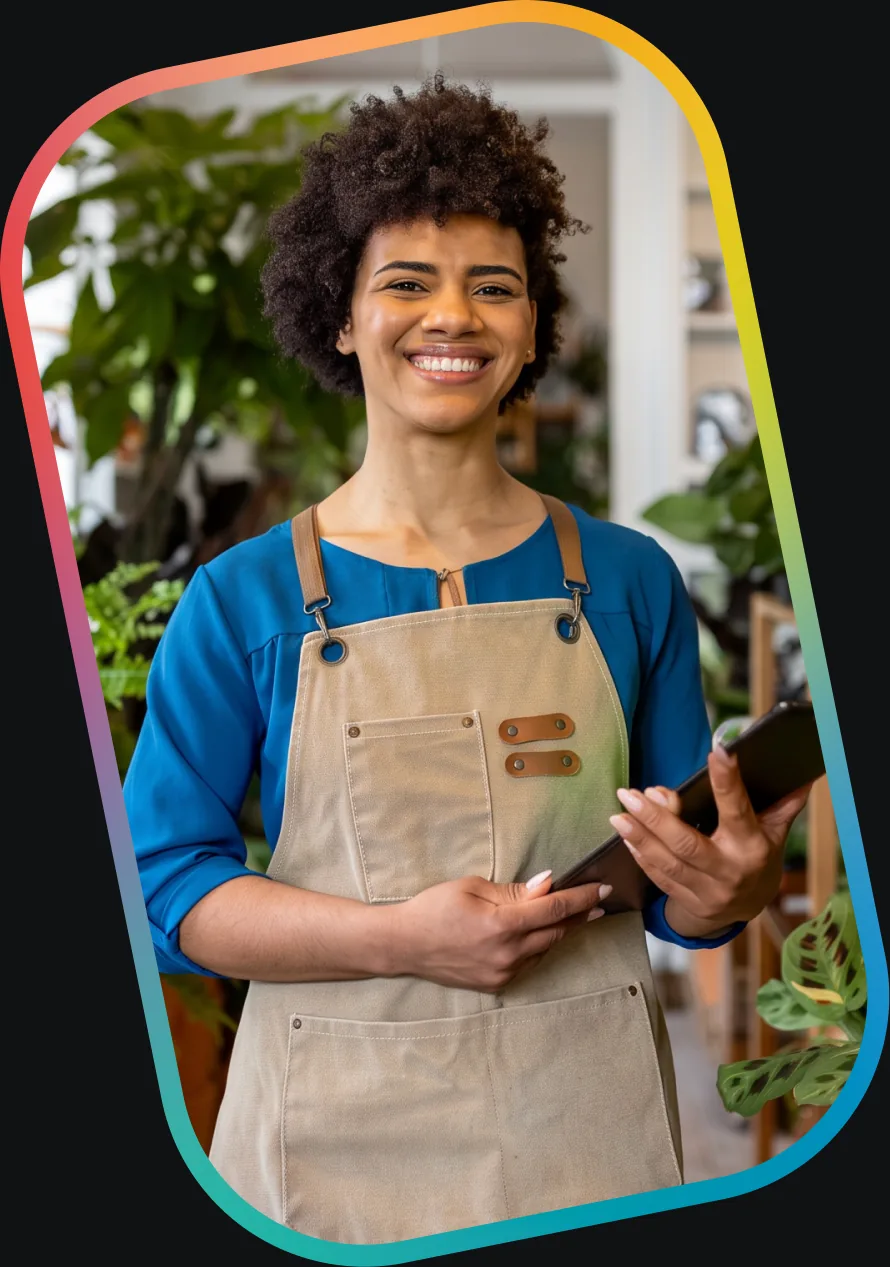 A small-business owner in an apron, holding a tablet in her shop.